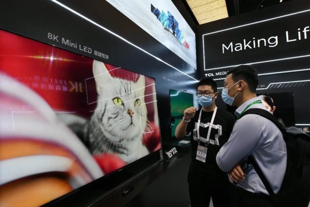 A staff member introduces a smart 8K television to a visitor at the 2021 World UHD Video Industrial Conference held in Guangzhou, south China's Guangdong province, May 10, 2021. (Photo by Xu Jianmei/People's Daily)